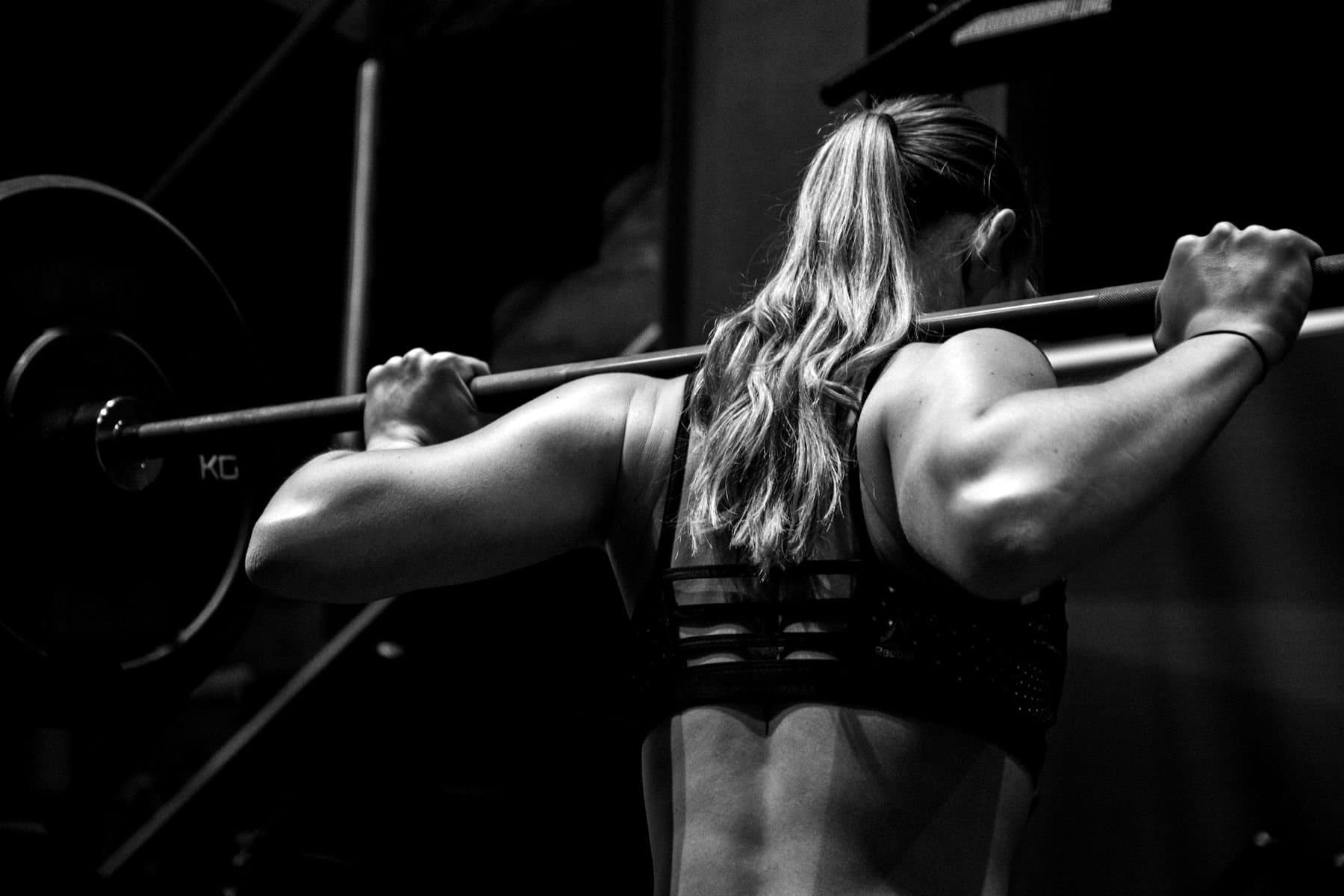 Una donna prepara uno squat con il bilanciere sulle spalle, in una palestra in penombra.